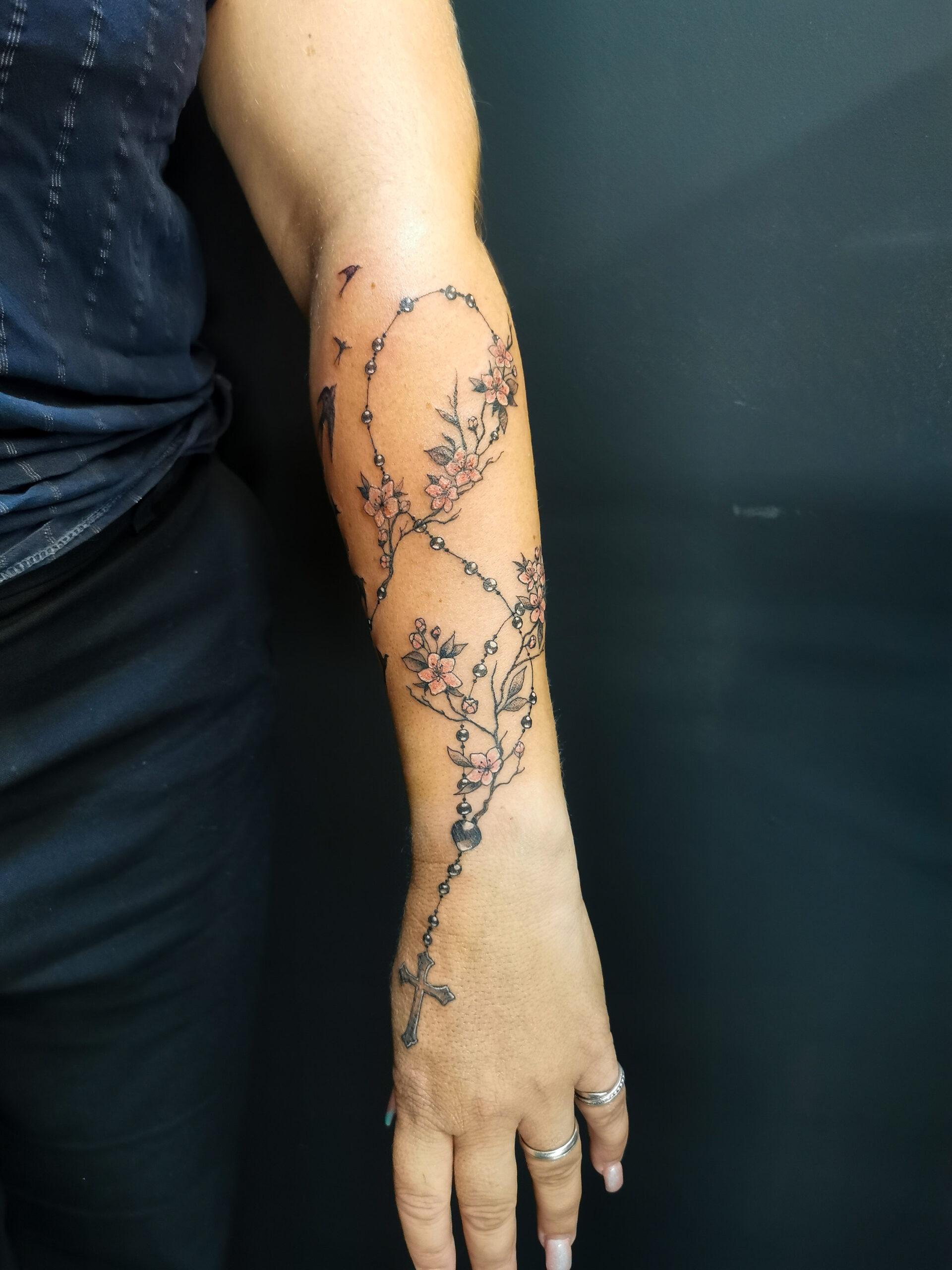 Photo d'un tatouage sur tout l'avant bras représentant un chapelet avec la croix sur la main ainsi que des branches de cerisiers et 3 oiseaux qui s'envolent en réaliste