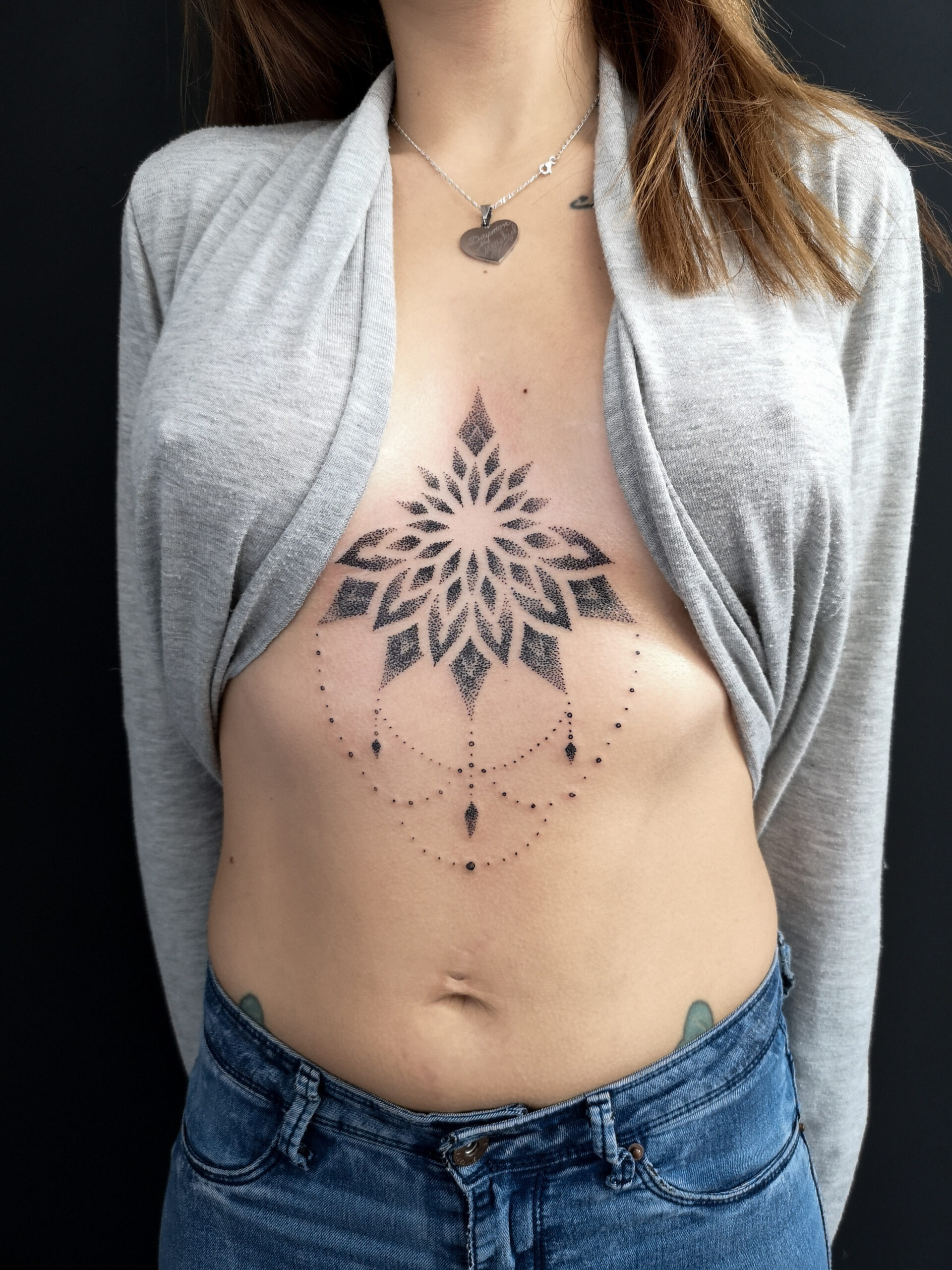 Photo d'un tatouage entre les seins en mandala dot avec des perles en noir et gris