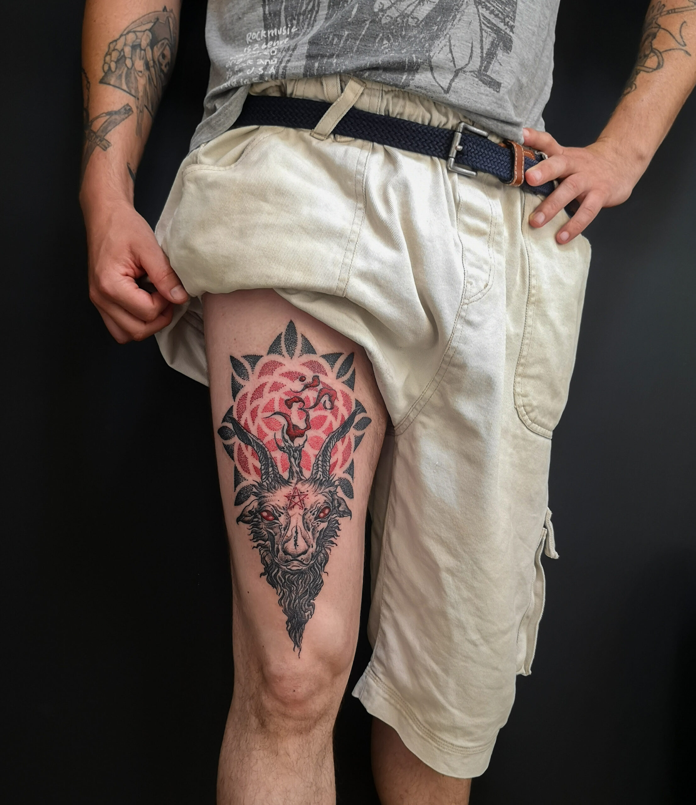 Photo d'un tatouage sur la cuisse représentant une tête de bouc avec une bougie au-dessus du crane dont la fumée forme un "ohm" avec en fond un mandala en dégradé de noir et rouge