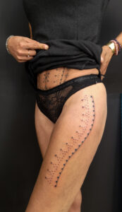 Photo représentant une femme du buste au genoux avec un tatouage sur tout le ventre et la cuisse représentant des motifs berbères