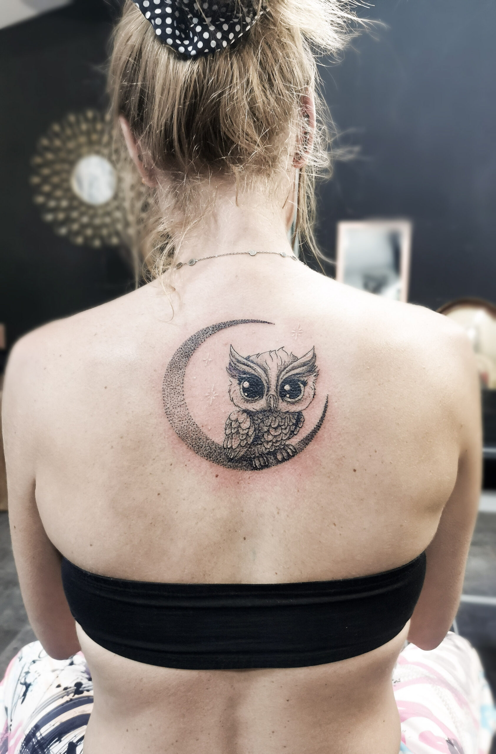 Photo d'un tatouage sur le dos représentant un hibou un peu cartoon sur une lune en dotwork