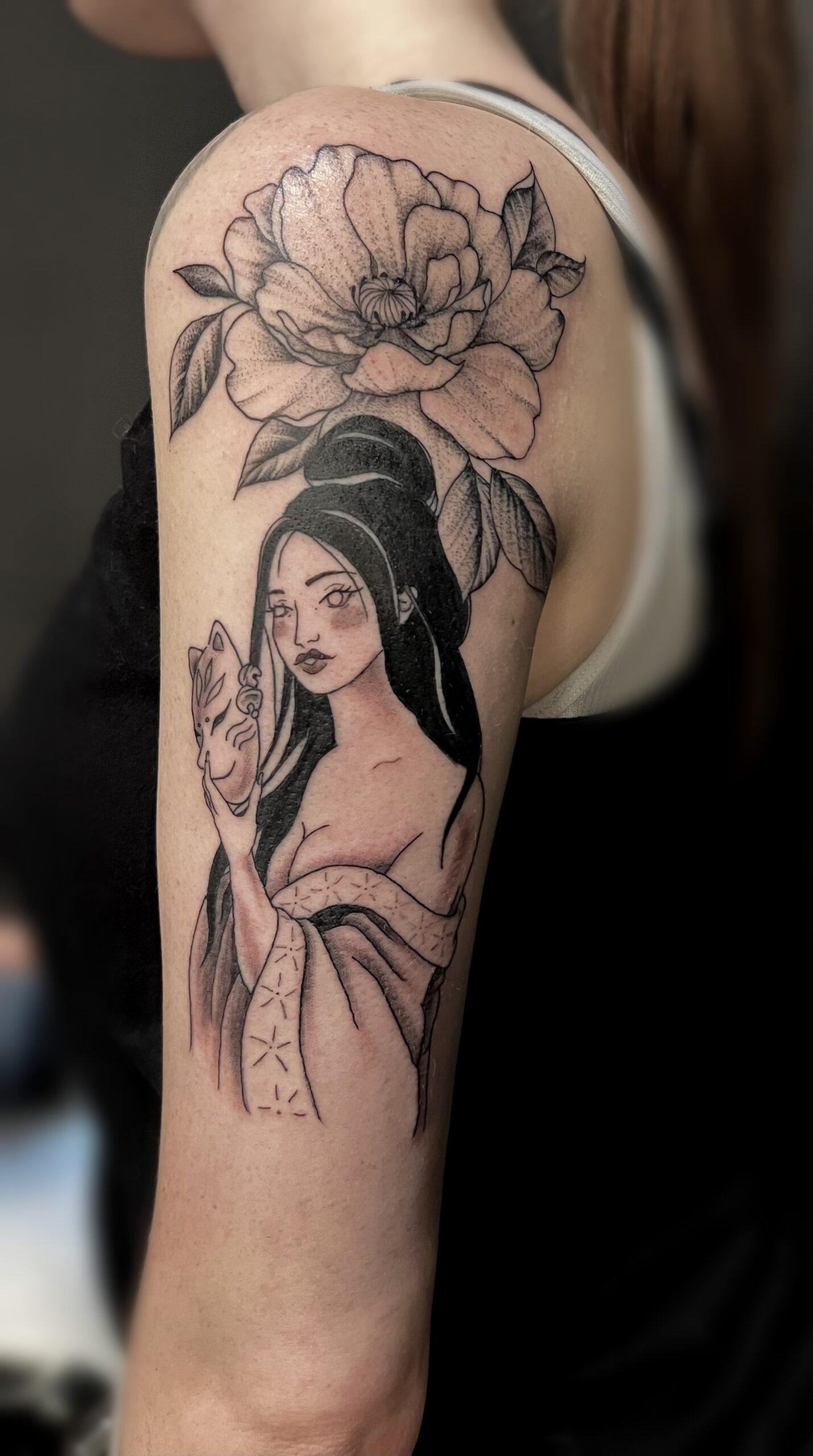 Photo d'un tatouage sur le bras représentant une geisha avec un masque de chat en main ainsi qu'une pivoine au-dessus d'elle